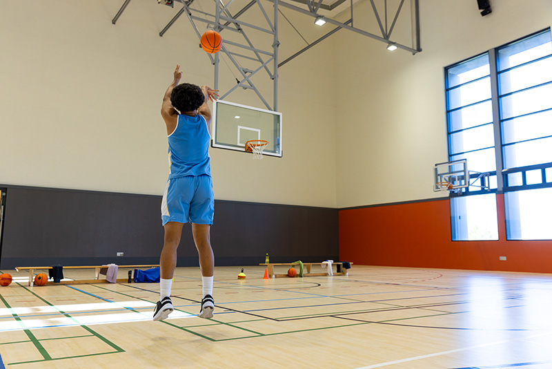 Biracial male basketball player wearing blue sports clothes and shooting basketball at gym. Sport, activity and lifestyle, unaltered, copy space.